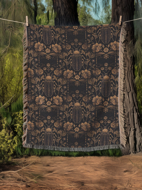 Black cotton throw blanket featuring woven bronze beetles and botanical motifs with multicolored fringe trim.